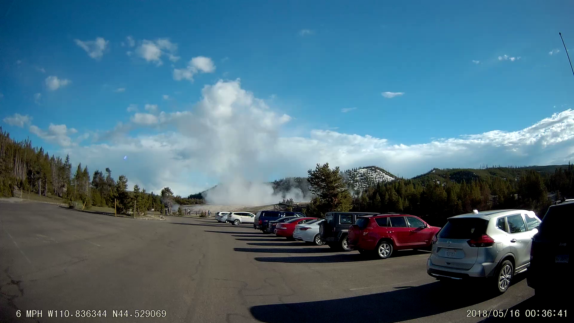a screencap from dashcam footage showing a geyser erupting from a parking lot in Yellowstone National Park
